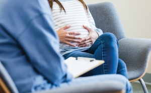 An unrecognizable expectant mom sitting in a chair puts her hands on her belly as she shares her worries about her baby with the unrecognizable therapist. 